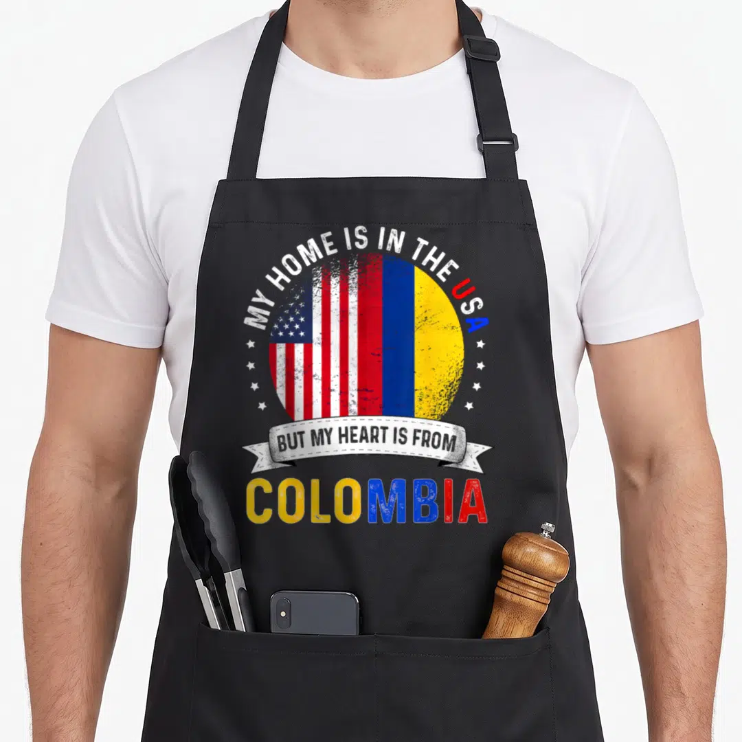 Colombian american flag apron - Combined USA and Colombia flag circle with MY HOME IS IN THE USA BUT MY HEART IS — shown on a black cotton canvas apron against a white background