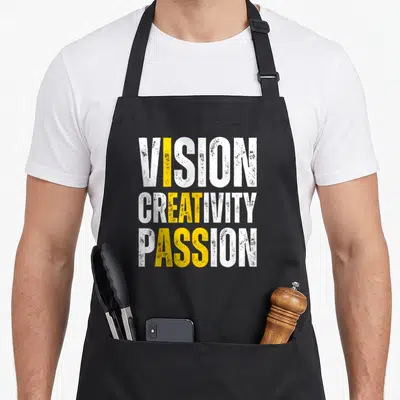Vision meme apron - Stacked white and yellow text VISION CREATIVITY PASSION on black fabric — shown on a black cotton canvas apron against a white background
