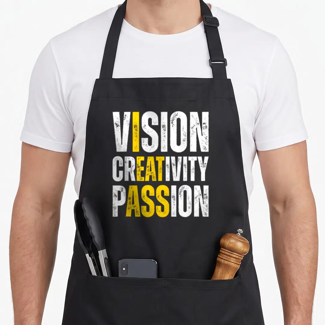 Vision meme apron - Stacked white and yellow text VISION CREATIVITY PASSION on black fabric — shown on a black cotton canvas apron against a white background
