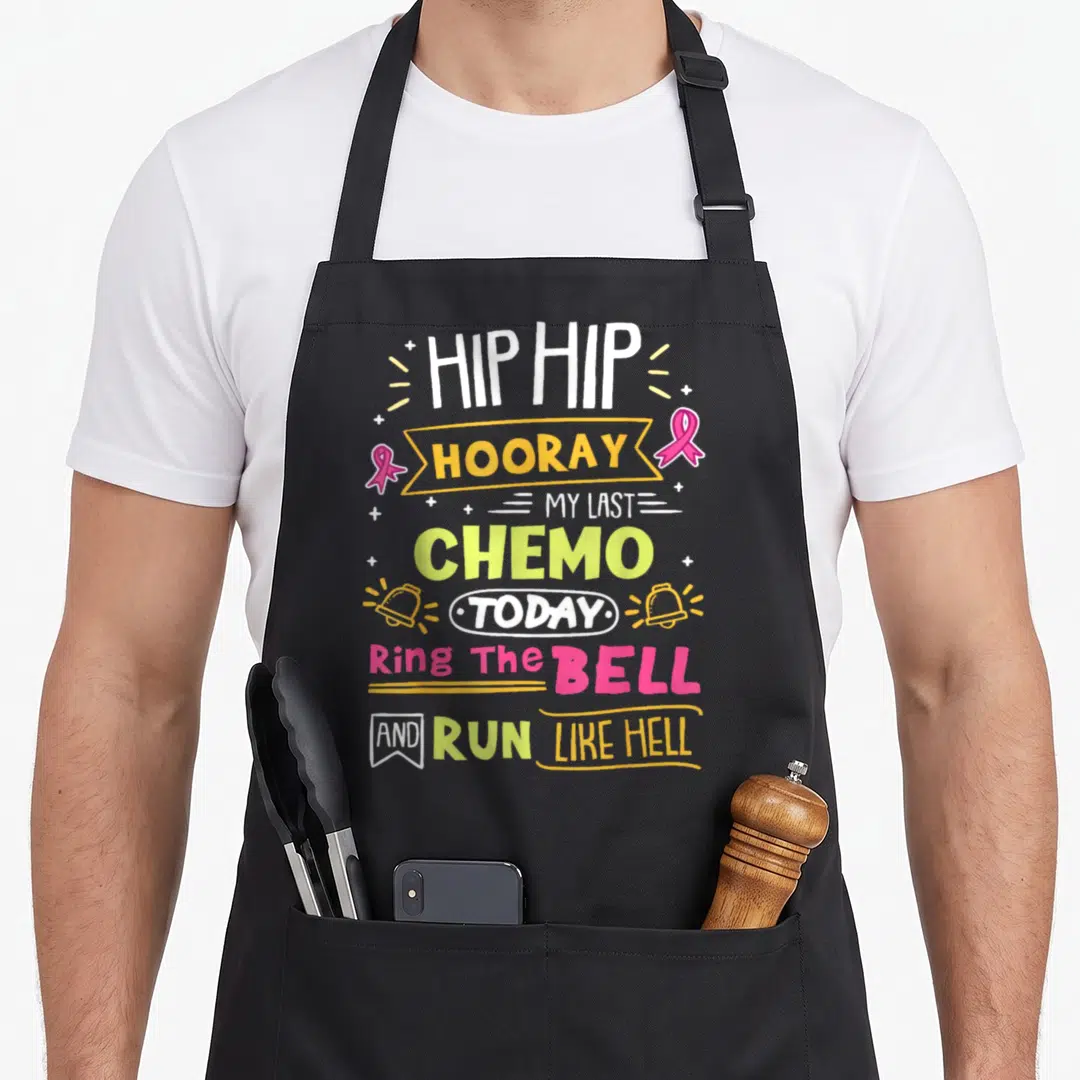 Chemo ring apron - Stacked text Hip Hooray My Last Chemo Today with pink ribbons and bells in white yellow pink lime — shown on a black cotton canvas apron against a white background