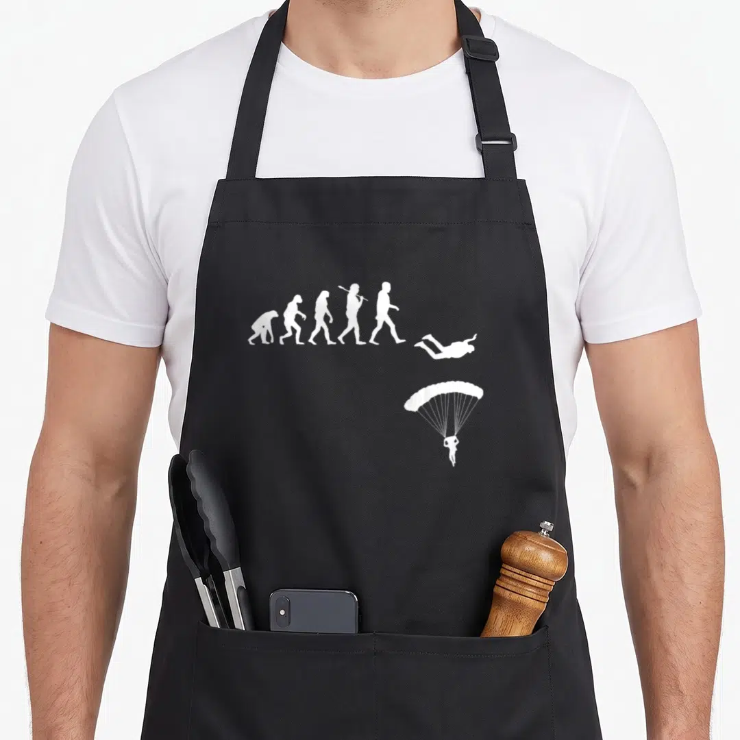 Evolution skydiving apron - White silhouette sequence of human evolution ending with a skydiver and parachute — shown on a black cotton canvas apron against a white background