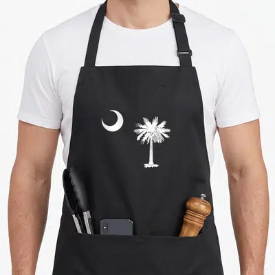 Moon pride apron - White crescent moon next to a palm tree in minimalist style — shown on a black cotton canvas apron against a white background