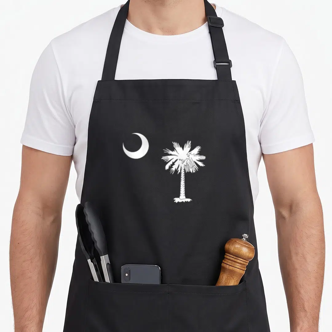 Moon pride apron - White crescent moon next to a palm tree in minimalist style — shown on a black cotton canvas apron against a white background