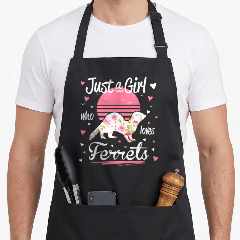 Funny love ferret apron - Just a Girl who loves Ferrets text around floral ferret silhouette and pink sun — shown on a black cotton canvas apron against a white background