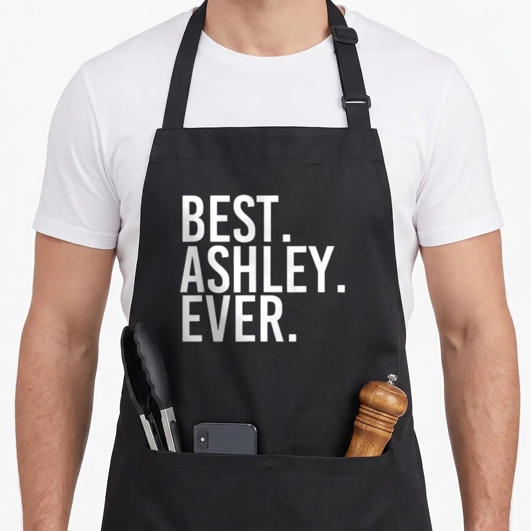 Ashley joke apron - White stacked text BEST. ASHLEY. EVER. on dark background — shown on a black cotton canvas apron against a white background