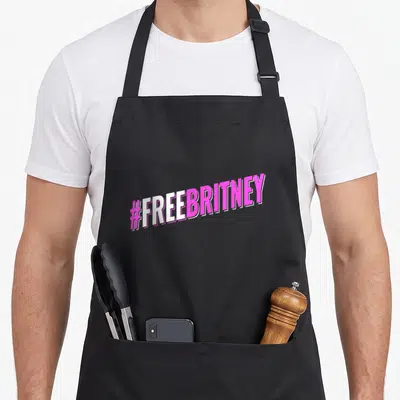 Hashtag brittany apron - #FREEBRITNEY pink and white tilted typography text only — shown on a black cotton canvas apron against a white background
