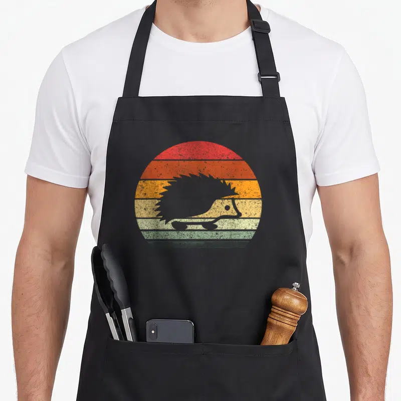 Sunset hedgehog mom apron - Grey hedgehog silhouette against red orange yellow green grey striped retro sun — shown on a black cotton canvas apron against a white background
