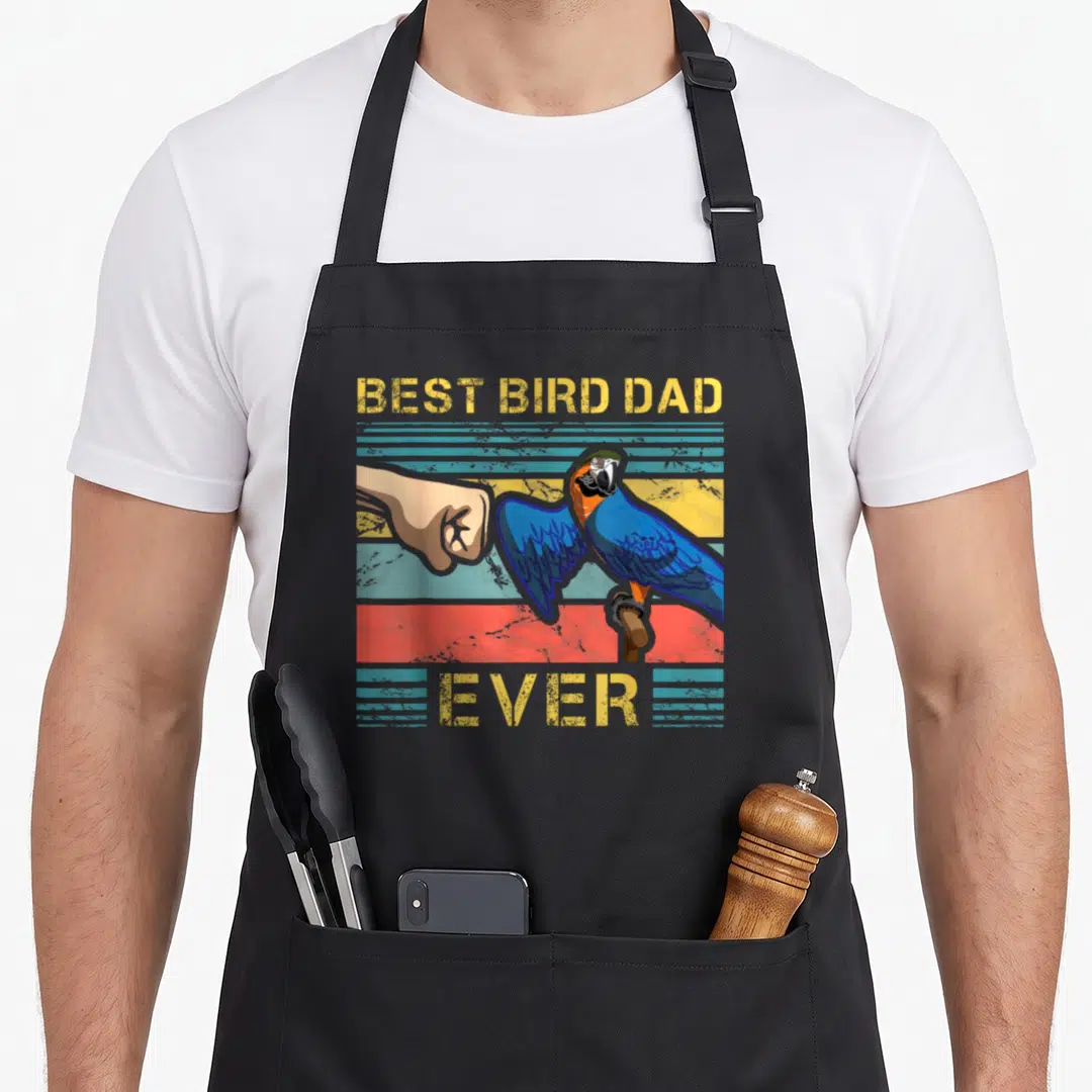 Enthusiast bird apron - Blue parrot fist bumping tan hand with Best Bird Dad Ever text on striped yellow blue red — shown on a black cotton canvas apron against a white background