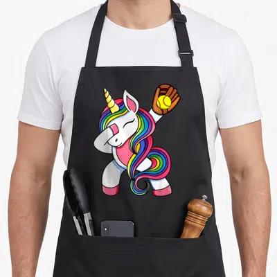 Softball unicorn apron - Cartoon white unicorn dabbing with brown glove holding yellow ball — shown on a black cotton canvas apron against a white background