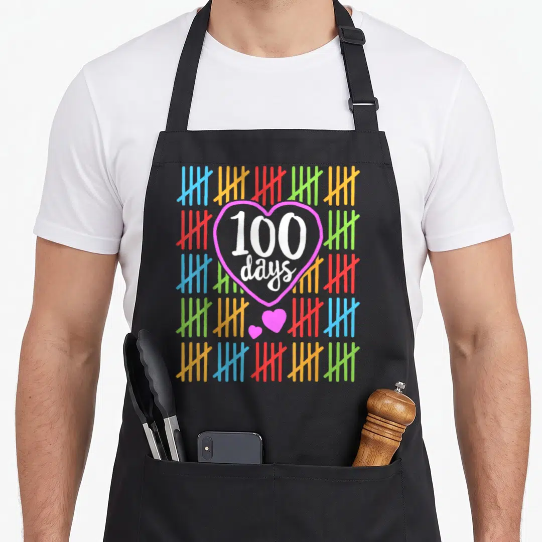 Counting teacher apron - 100 days text in pink heart surrounded by colored tally marks — shown on a black cotton canvas apron against a white background