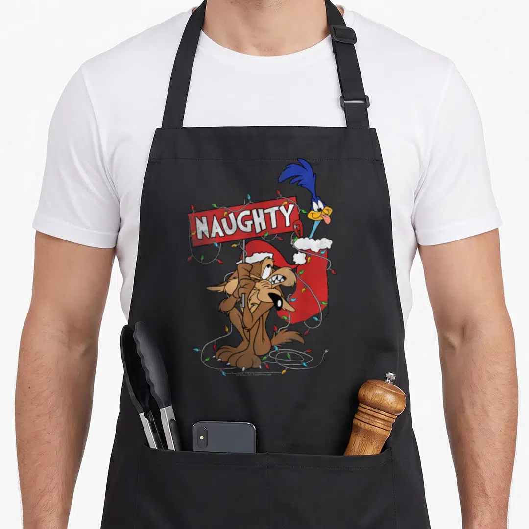 Road christmas apron - Wile E. Coyote holds red NAUGHTY sign with Road Runner in stocking and Christmas lights — shown on a black cotton canvas apron against a white background