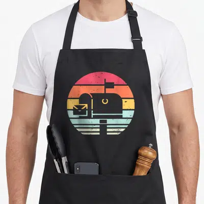 Mail carrier postal aprons - Retro striped circle with white mailbox and envelope silhouette — shown on a black cotton canvas apron against a white background
