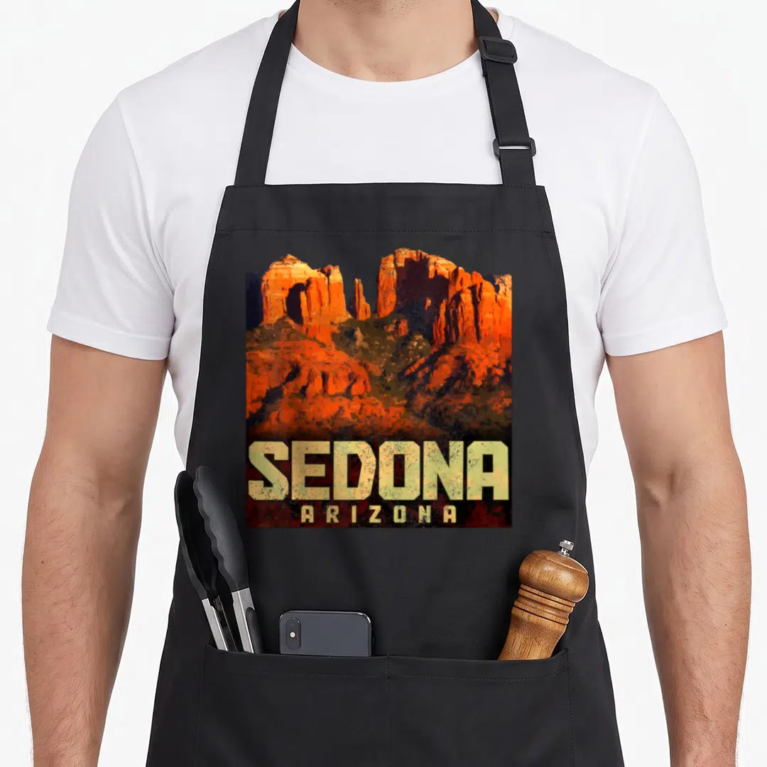 Sedona pride apron - Rectangular red rock mountains with SEDONA ARIZONA text in yellow and orange retro style — shown on a black cotton canvas apron against a white background