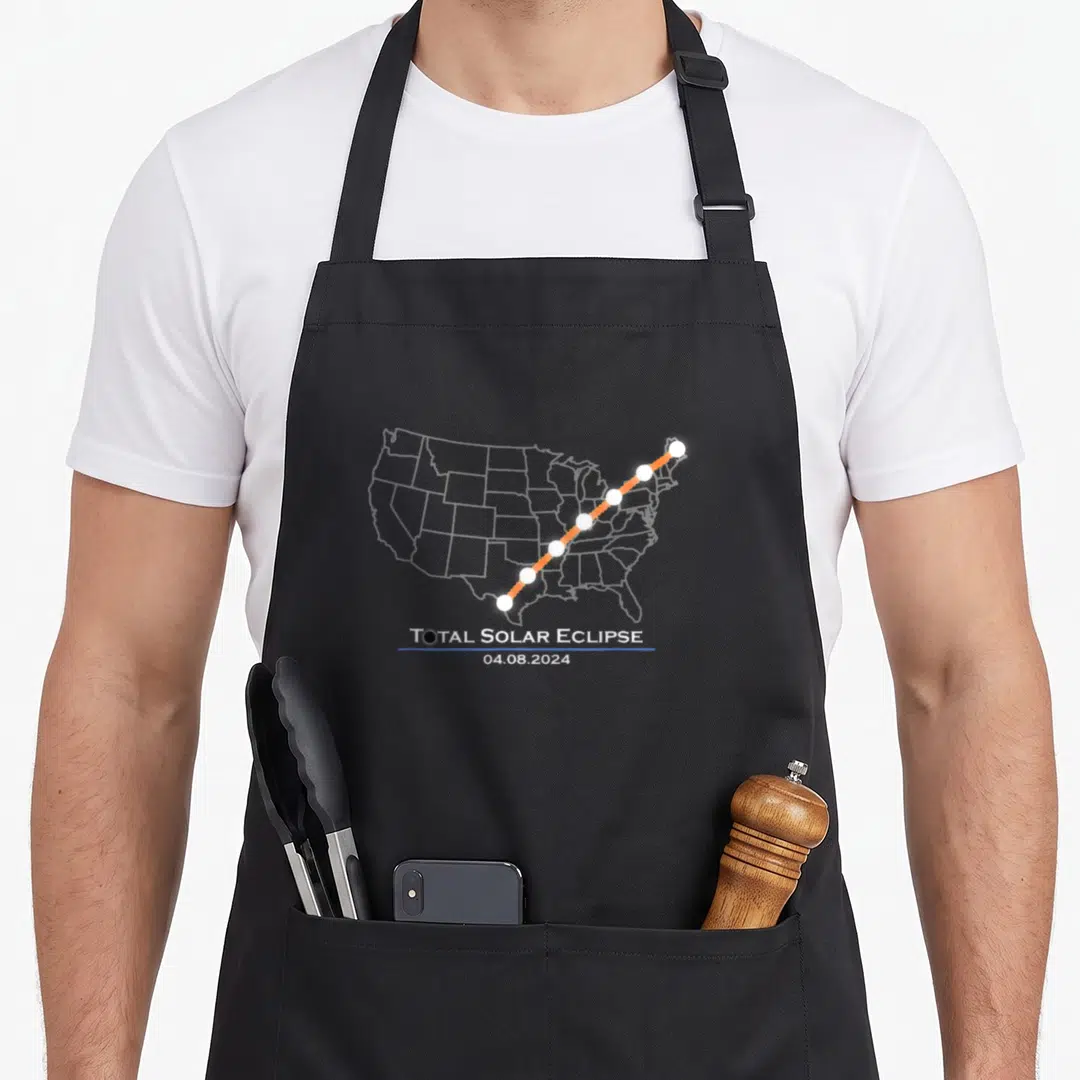 Totality total april apron - Orange eclipse path with white circles over grey US map and date text — shown on a black cotton canvas apron against a white background