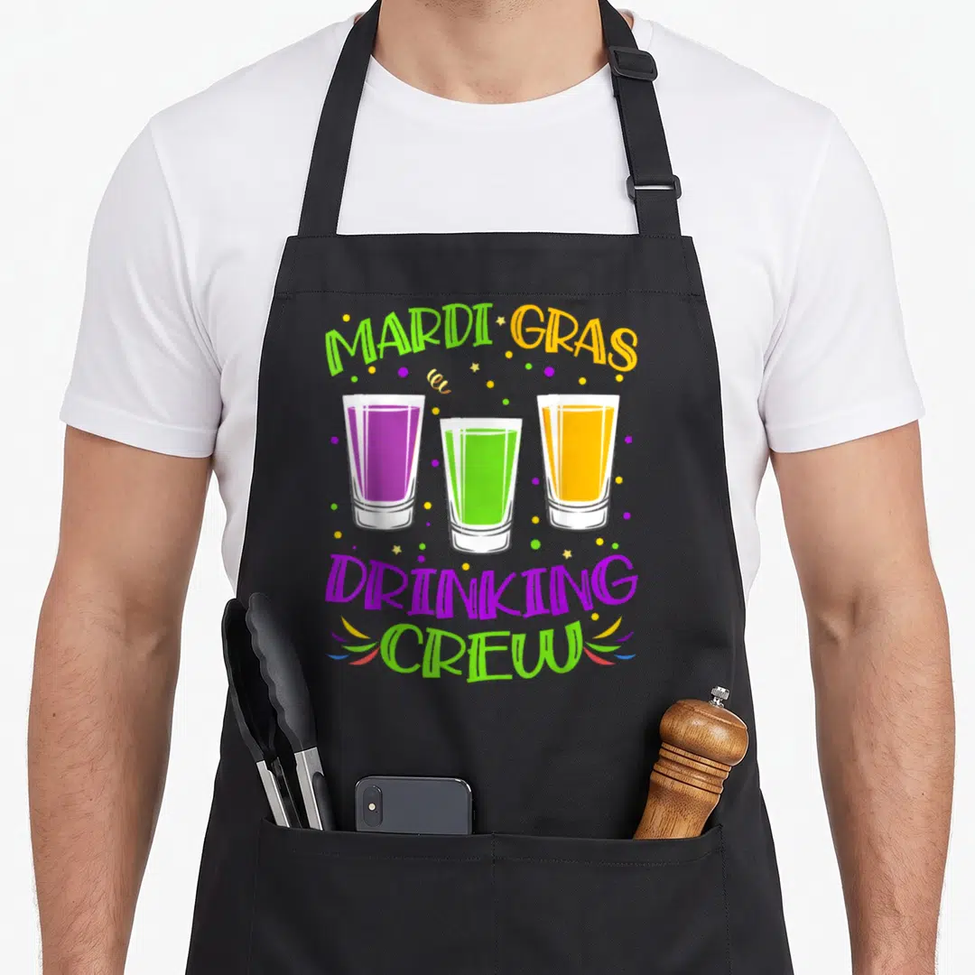 Drinking fat chef apron - Three shot glasses in purple, lime green, orange with MARDI GRAS DRINKING CREW text — shown on a black cotton canvas apron against a white background