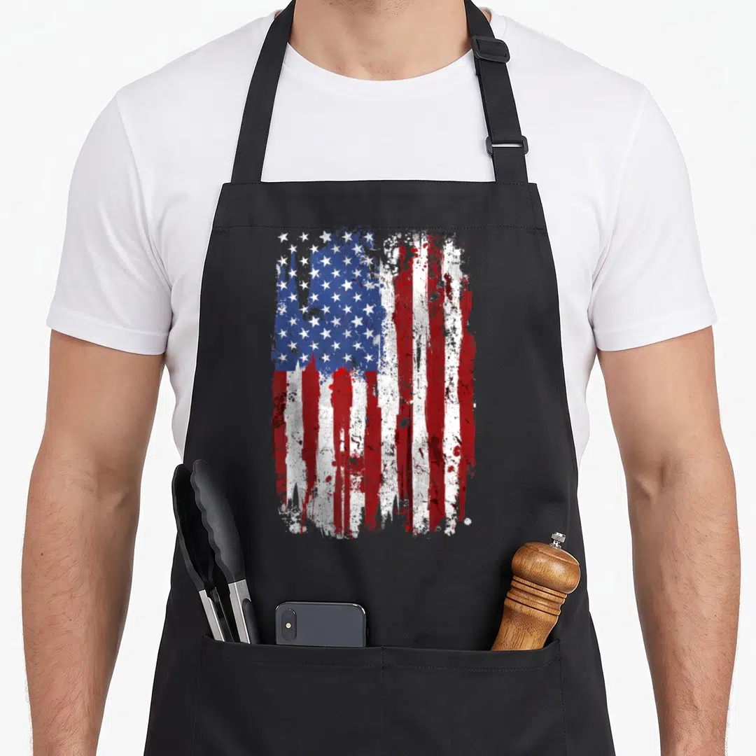 Flag patriotic 4th of july apron - Distressed USA flag illustration in red white and blue with splatter effects — shown on a black cotton canvas apron against a white background