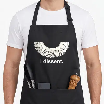 Ruth i love football apron - White lace collar graphic above the text I dissent — shown on a black cotton canvas apron against a white background