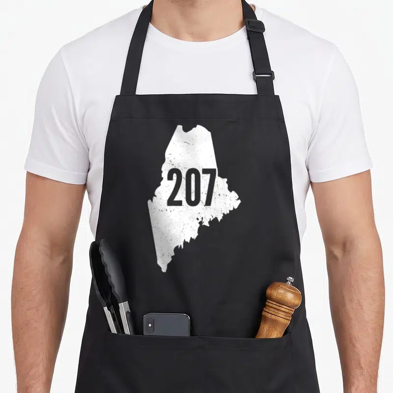 Maine outline of an apron - Distressed white Maine map shape with grey 207 number centered on front panel — shown on a black cotton canvas apron against a white background