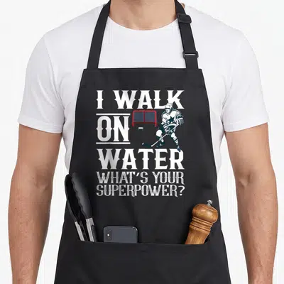 Walk hockey ice apron - I Walk on Water text with hockey player red goal and puck — shown on a black cotton canvas apron against a white background