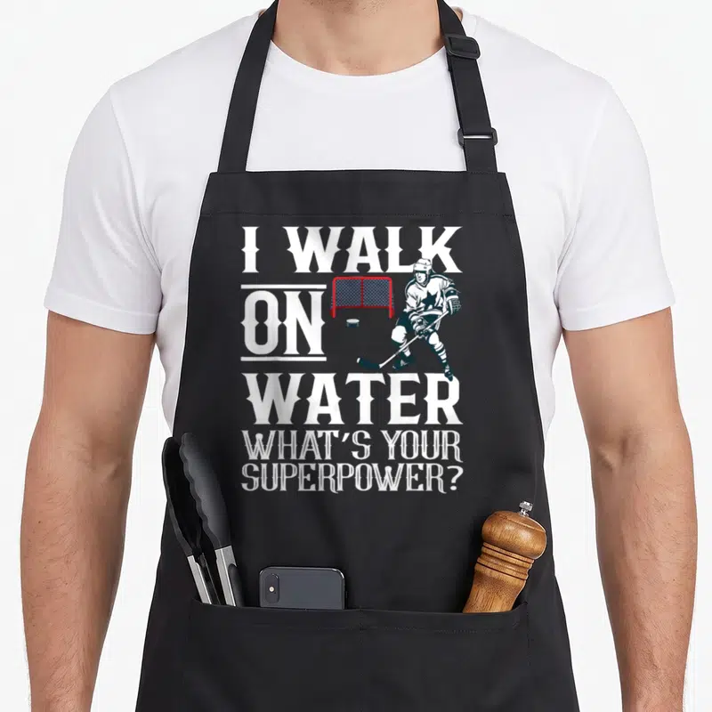 Walk hockey ice apron - I Walk on Water text with hockey player red goal and puck — shown on a black cotton canvas apron against a white background