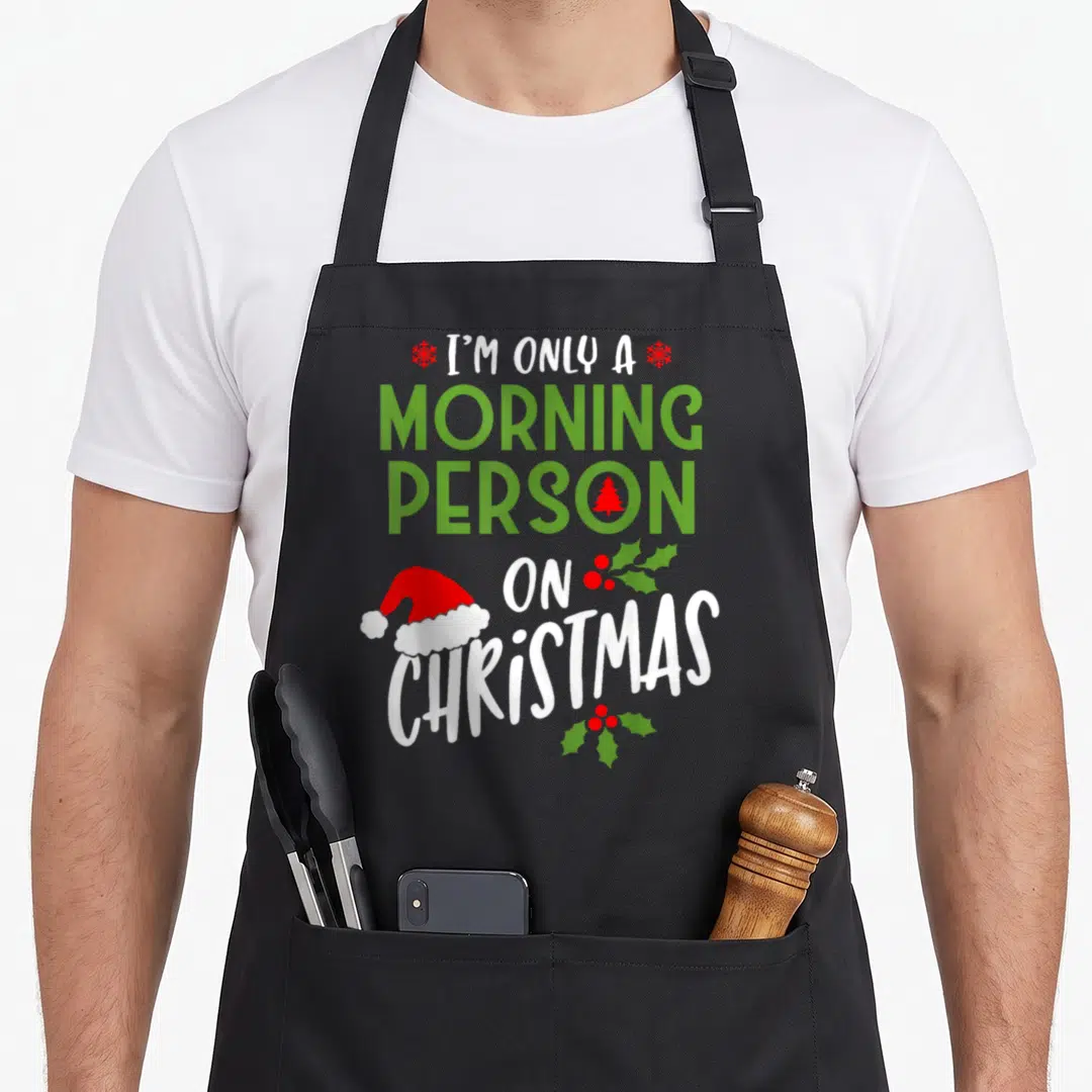 Cute morning women's christmas apron - Stacked text I'm Only a Morning Person on Christmas with Santa hat and holly — shown on a black cotton canvas apron against a white background