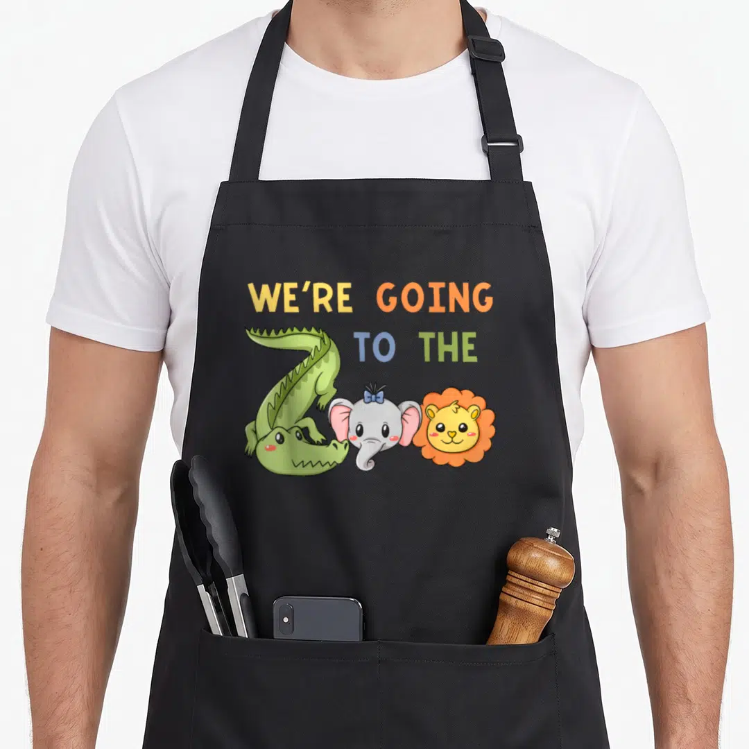 Crocodile lion apron - Cartoon green crocodile grey elephant and orange lion below stacked text WE'RE GOING — shown on a black cotton canvas apron against a white background