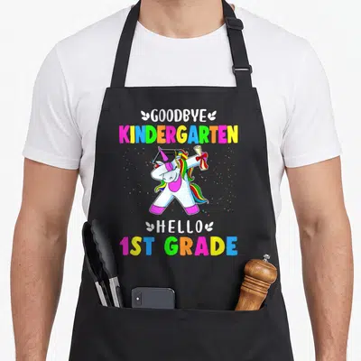 Goodbye kindergarten unicorn apron - Dabbing unicorn with cap and diploma surrounded by rainbow text and confetti — shown on a black cotton canvas apron against a white background