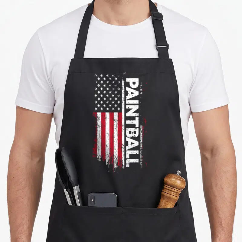 Paintball american flag apron - Distressed USA flag with vertical white PAINTBALL text on red white and blue background — shown on a black cotton canvas apron against a white background