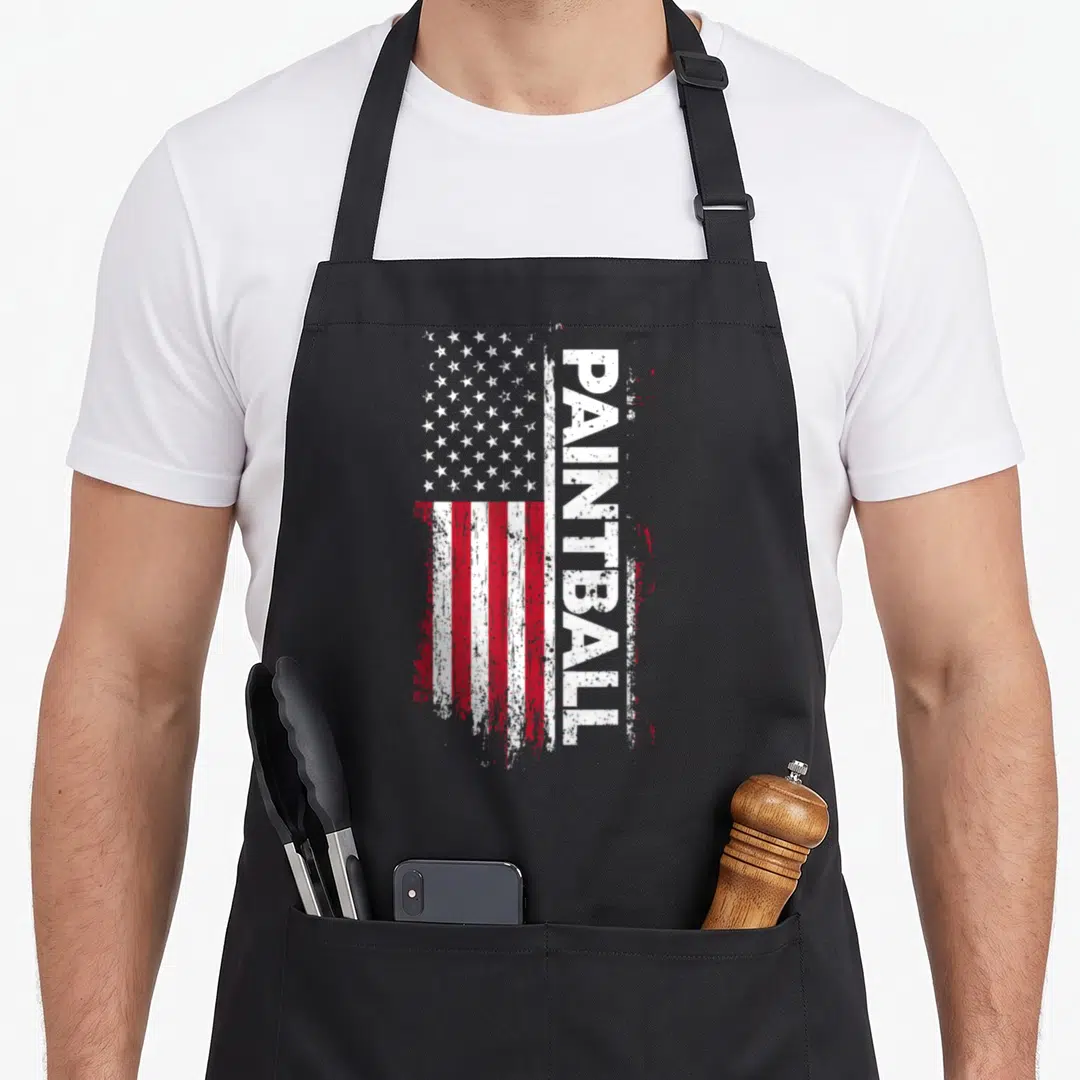 Paintball american flag apron - Distressed USA flag with vertical white PAINTBALL text on red white and blue background — shown on a black cotton canvas apron against a white background