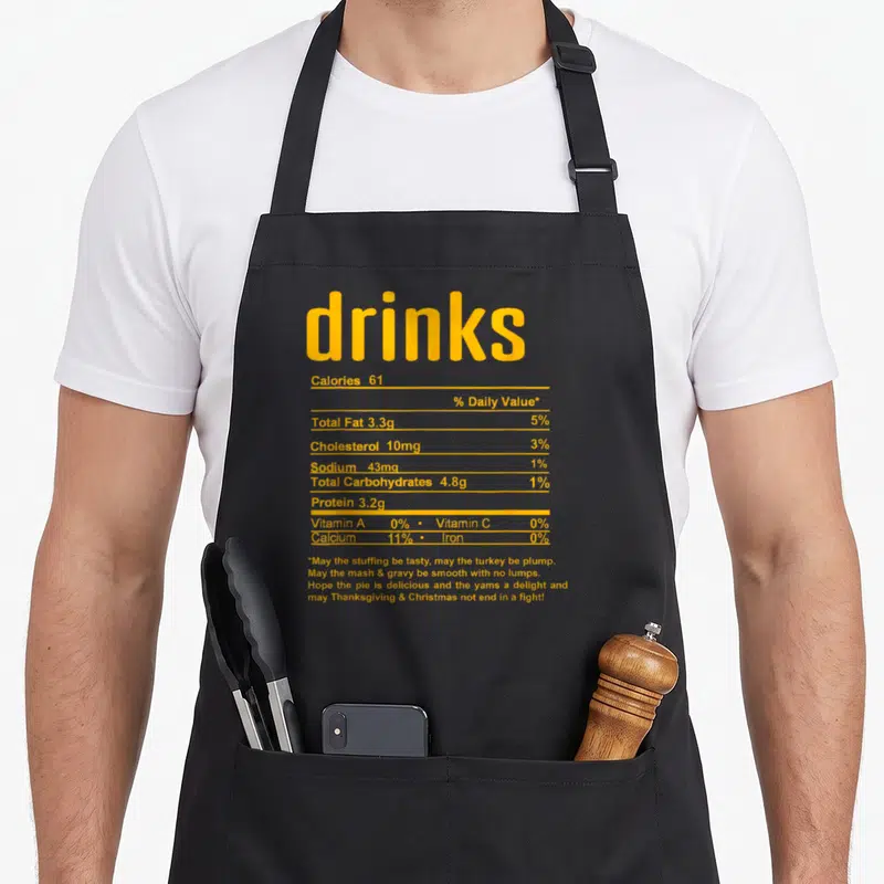 Fact thanksgiving aprons - Yellow nutrition label text for drinks listing calories and holiday wishes — shown on a black cotton canvas apron against a white background