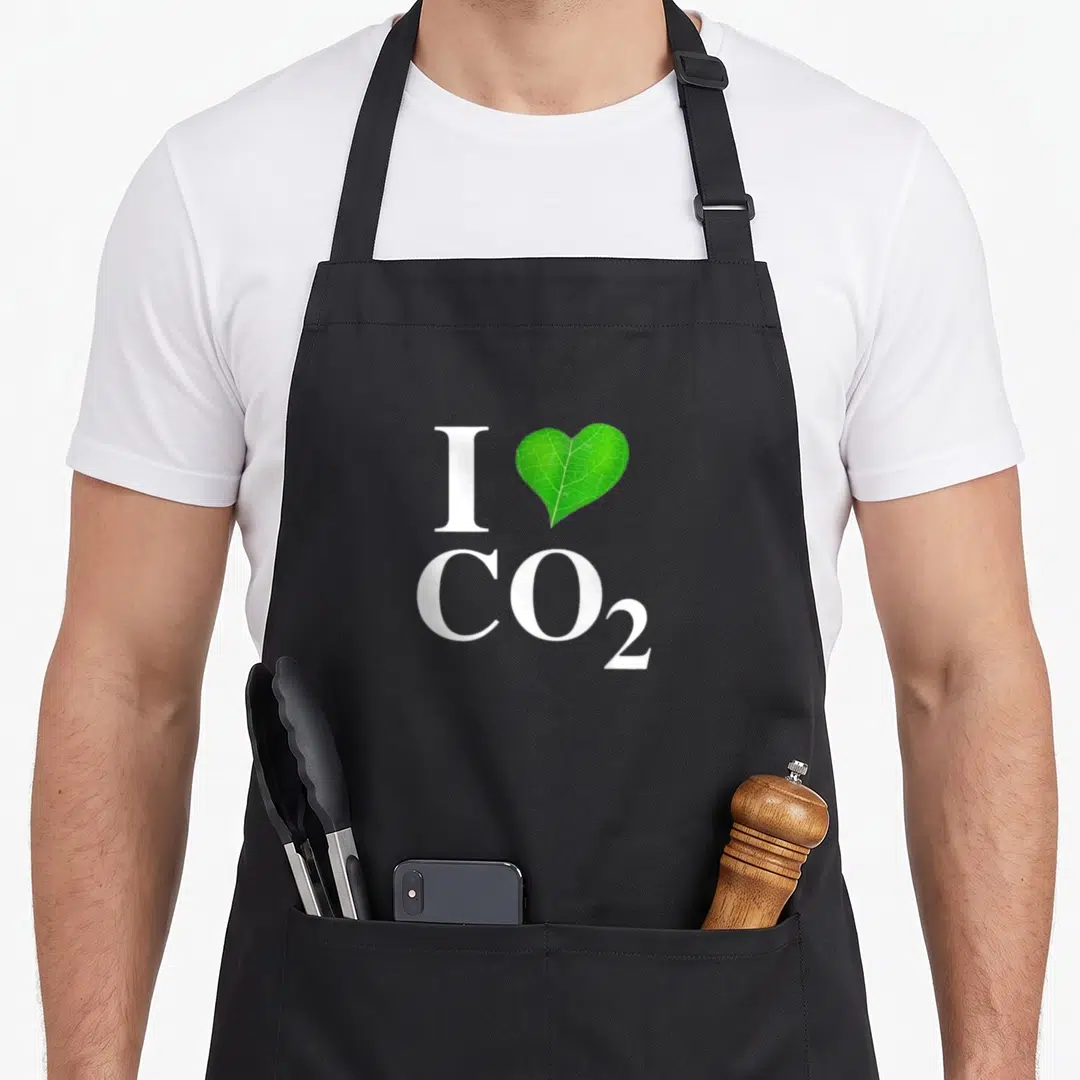 Co2 change apron - White I and CO2 text with a green heart-shaped leaf in the center — shown on a black cotton canvas apron against a white background