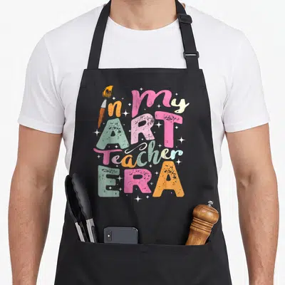 Era teaching teacher apron - Stacked colorful text in my ART Teacher ERA with paintbrush and white stars — shown on a black cotton canvas apron against a white background