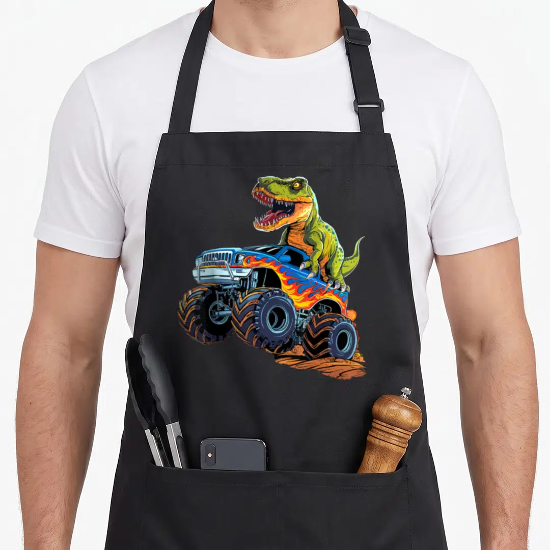 Monster dinosaur truck apron - Green T-Rex leaning over blue monster truck with flame decals on brown dirt — shown on a black cotton canvas apron against a white background