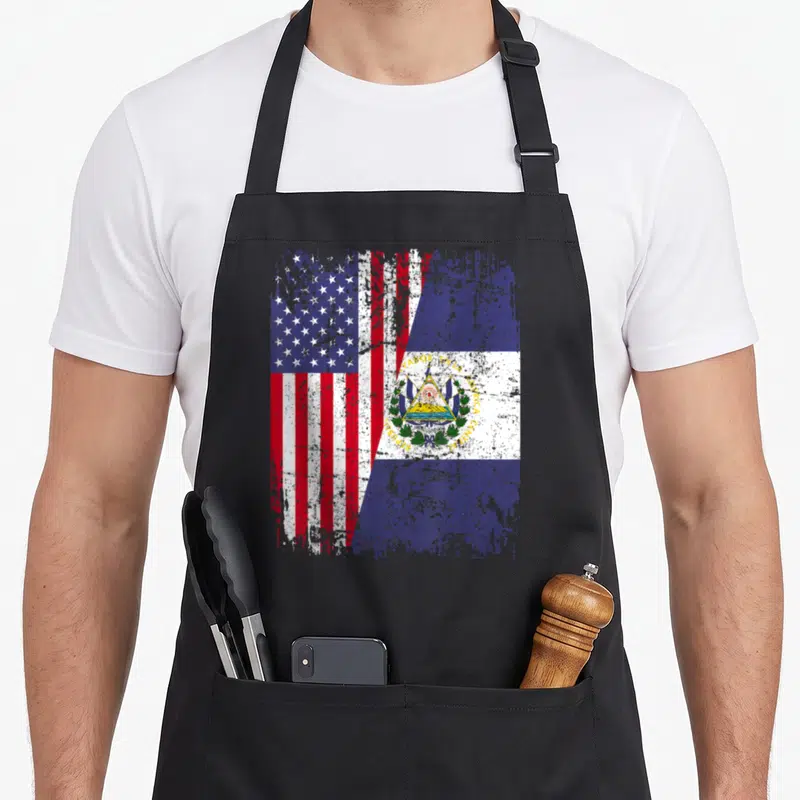 Root salvadoran apron - Merged US and El Salvador flags with distressed texture and printed text — shown on a black cotton canvas apron against a white background