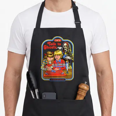 Steven ghost apron - Two children at ouija board with skeleton. Text Let's Talk to Ghosts ACTIVITIES FOR CHILDREN retro — shown on a black cotton canvas apron against a white background