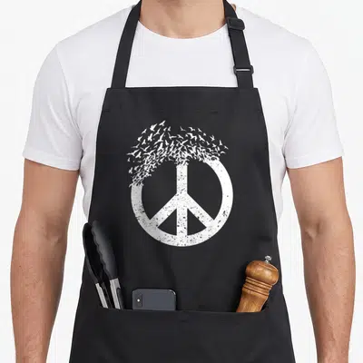 Peace bird apron - Distressed white peace symbol dissolving into a flock of flying birds — shown on a black cotton canvas apron against a white background