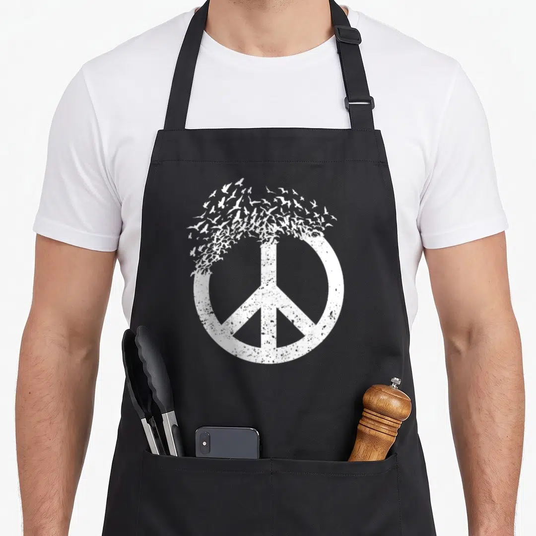 Peace bird apron - Distressed white peace symbol dissolving into a flock of flying birds — shown on a black cotton canvas apron against a white background