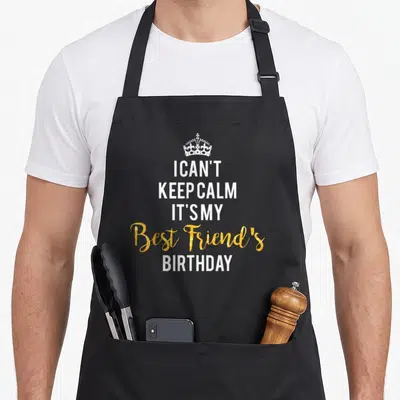 Cute birthday friends apron - White crown above stacked text I CAN'T KEEP CALM IT'S MY Best Friend's BIRTHDAY in gold — shown on a black cotton canvas apron against a white background
