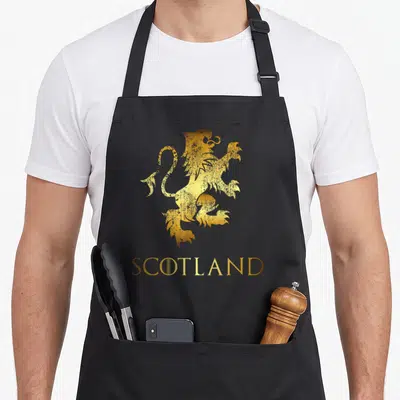 Scotland kilt apron - Gold gradient lion standing above SCOTLAND text in minimalist style — shown on a black cotton canvas apron against a white background