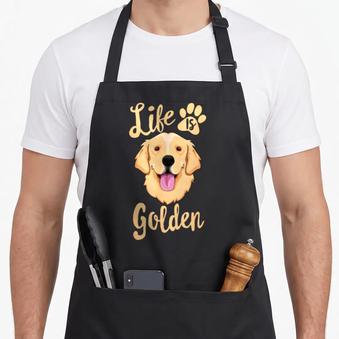 Owner golden retriever apron - Cartoon golden retriever head with Life is Golden text and paw print in peach — shown on a black cotton canvas apron against a white background
