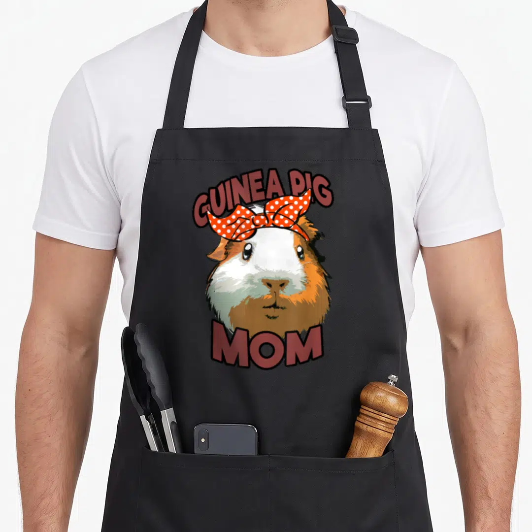 Funny cavy guinea pigs apron - Cartoon guinea pig head with orange polka dot bow and GUINEA PIG MOM text — shown on a black cotton canvas apron against a white background