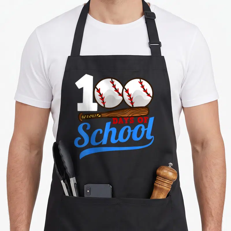 School baseball apron - 100 formed by one and two baseballs above a bat and Days of School text — shown on a black cotton canvas apron against a white background