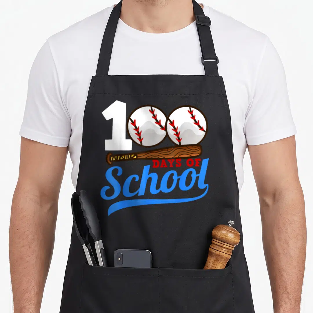 School baseball apron - 100 formed by one and two baseballs above a bat and Days of School text — shown on a black cotton canvas apron against a white background