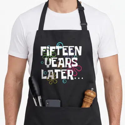 Fifteen birthday apron - FIFTEEN YEARS LATER... white text with green purple pink blue flower shapes and bubbles — shown on a black cotton canvas apron against a white background