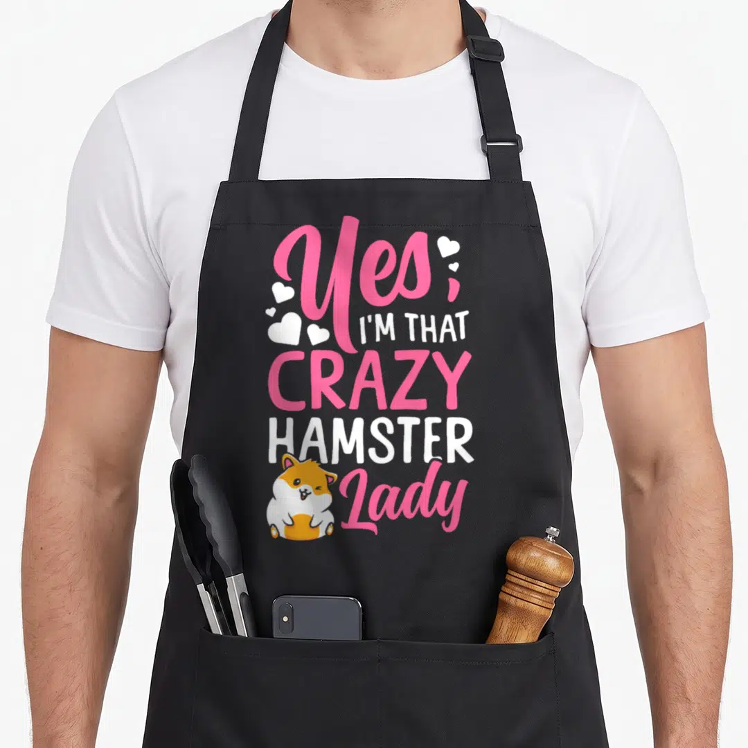 Cute comfort crazy hamster lady apron - Pink and white Yes I'm That Crazy Hamster Lady text with winking cartoon — shown on a black cotton canvas apron against a white background