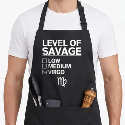 Virgo sign zodiac aprons - White text reading Level of Savage Low Medium Virgo with symbol below — shown on a black cotton canvas apron against a white background
