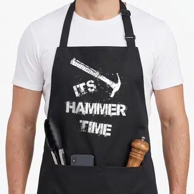 Hammer apron or apron - White distressed hammer above stacked ITS HAMMER TIME text — shown on a black cotton canvas apron against a white background