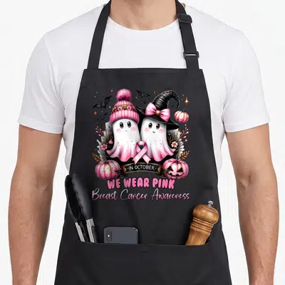 Ghost breast cancer awareness aprons - Two cartoon ghosts with pink ribbon and pumpkins wearing beanie and witch hat — shown on a black cotton canvas apron against a white background