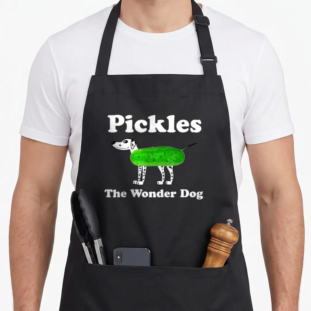 Pickle quirky apron - Cartoon spotted dog with green pickle torso and white text Pickles The Wonder Dog — shown on a black cotton canvas apron against a white background