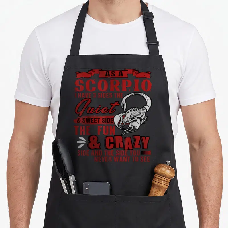 Funny scorpio birthday apron - Scorpion graphic with stacked text listing three personality sides in red and black — shown on a black cotton canvas apron against a white background